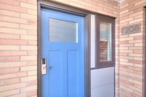 Une porte bleue avec une fenêtre, un interphone et le numéro de maison 208, le tout sur un mur de briques.