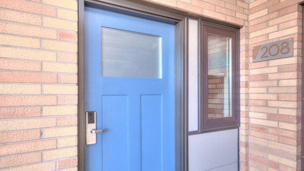 Eine blaue Tür mit Fenster, Klingel und einer Ziegelwand mit Hausnummer.