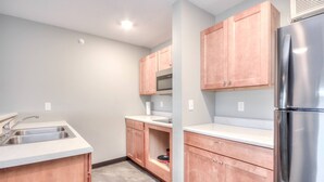 A kitchen with a stainless steel refrigerator, wooden cabinets, a microwave, and a sink. - 1BR with 2 beds and a kitchen on the 2nd floor (Rapid City)