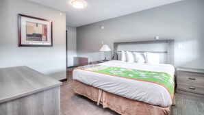 A hotel room with a bed, bedside table, lamp, and a framed picture on the wall.