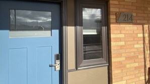 A blue door with a window, a doorbell, and a mailbox on a brick wall with a number plate.