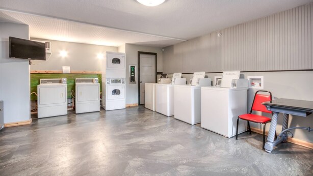 A laundry room with multiple washing machines, a television, and a red chair.