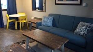 A living room with a blue sofa, a wooden coffee table, a yellow chair, a small table, and a framed picture on the wall.