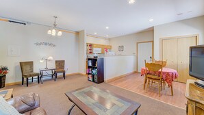 A living room with a sofa, two chairs, a coffee table, a TV, and a kitchen area with cabinets and a refrigerator. - Large 1BR Condo Near Lake Pepin - Starshine (Pepin)