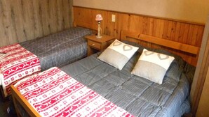 Ein Zimmer mit zwei Betten, jeweils mit gemusterten Bettbezügen, Holz-Kopfteilen und einem Nachttisch mit einer Lampe.