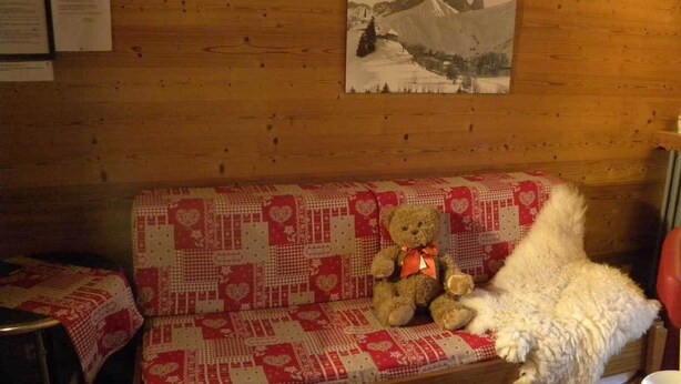Ein Holzhütten-Innenraum mit einer Couch, die mit einer roten und weißen Decke bedeckt ist, einem Teddybären und einem weißen, flauschigen Gegenstand.