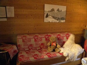A wooden cabin interior with a sofa covered in a red and white patterned blanket, a teddy bear, and a white fluffy object.