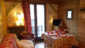 Ein gemütliches Zimmer mit einer Couch, einem Esstisch für vier Personen und einem Fernseher auf einer Kommode.