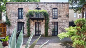 Edificio de ladrillo con un patio interior, destacando una puerta central, ventanas y un pequeño balcón con plantas.
