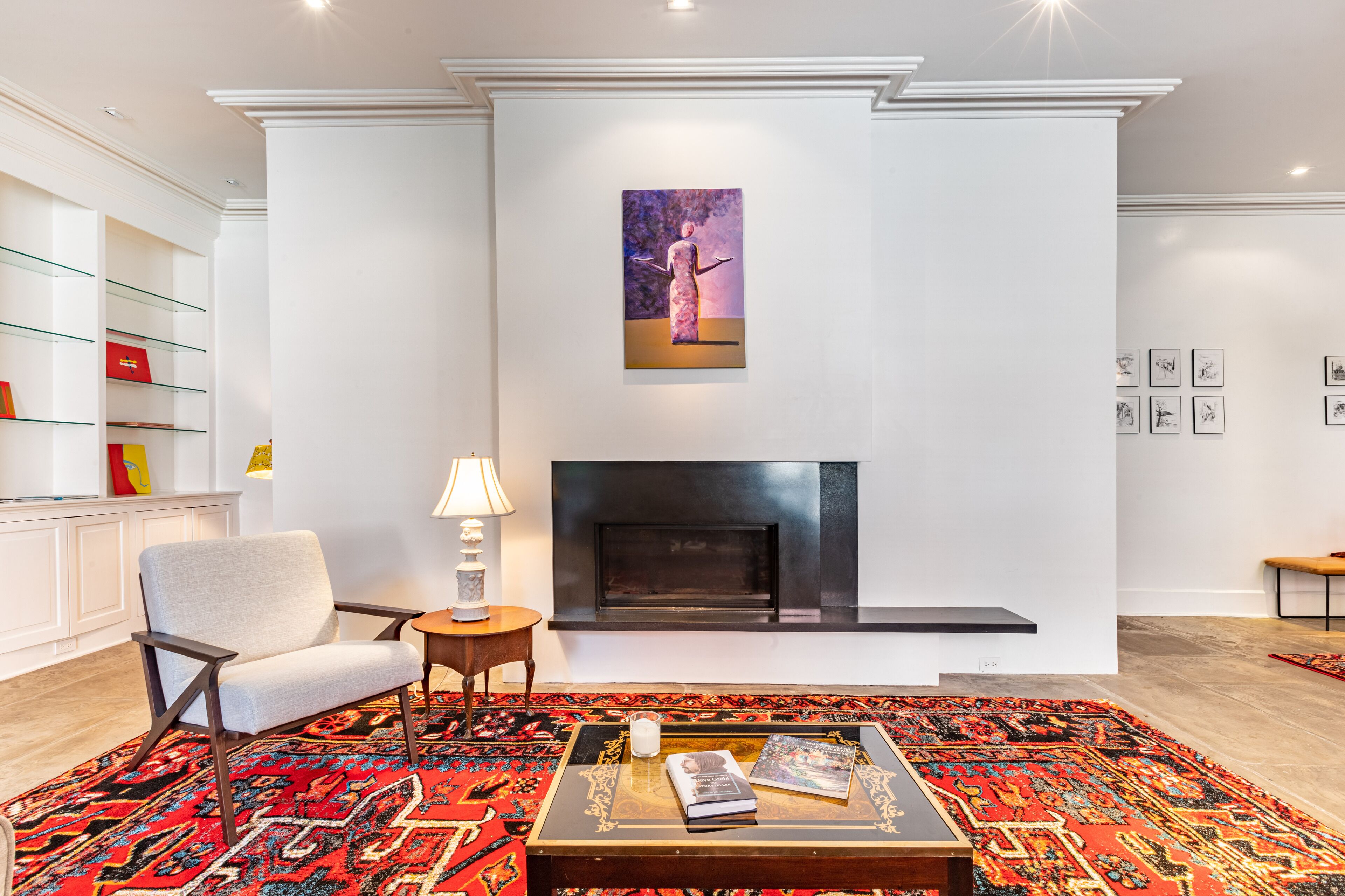 A modern living room with a fireplace, a comfortable armchair, a coffee table with books, and a colorful rug.
