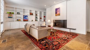 Una sala de estar moderna con un sofá, una chimenea y una estantería de vidrio con diversos objetos decorativos.