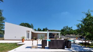Una casa moderna con patio, piscina y cocina exterior techada.