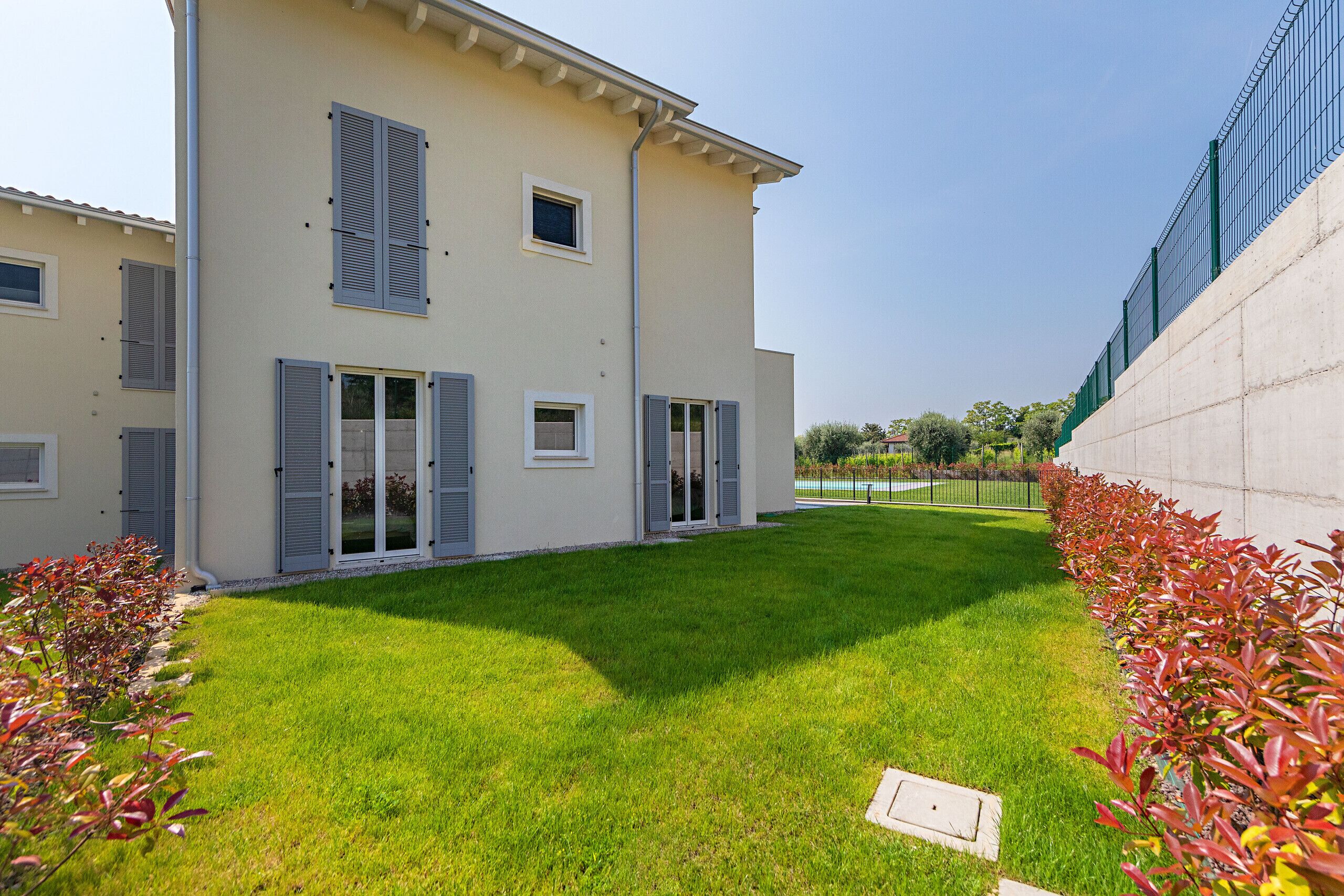 A two-story house with a well-maintained lawn, a concrete retaining wall, and a metal fence.