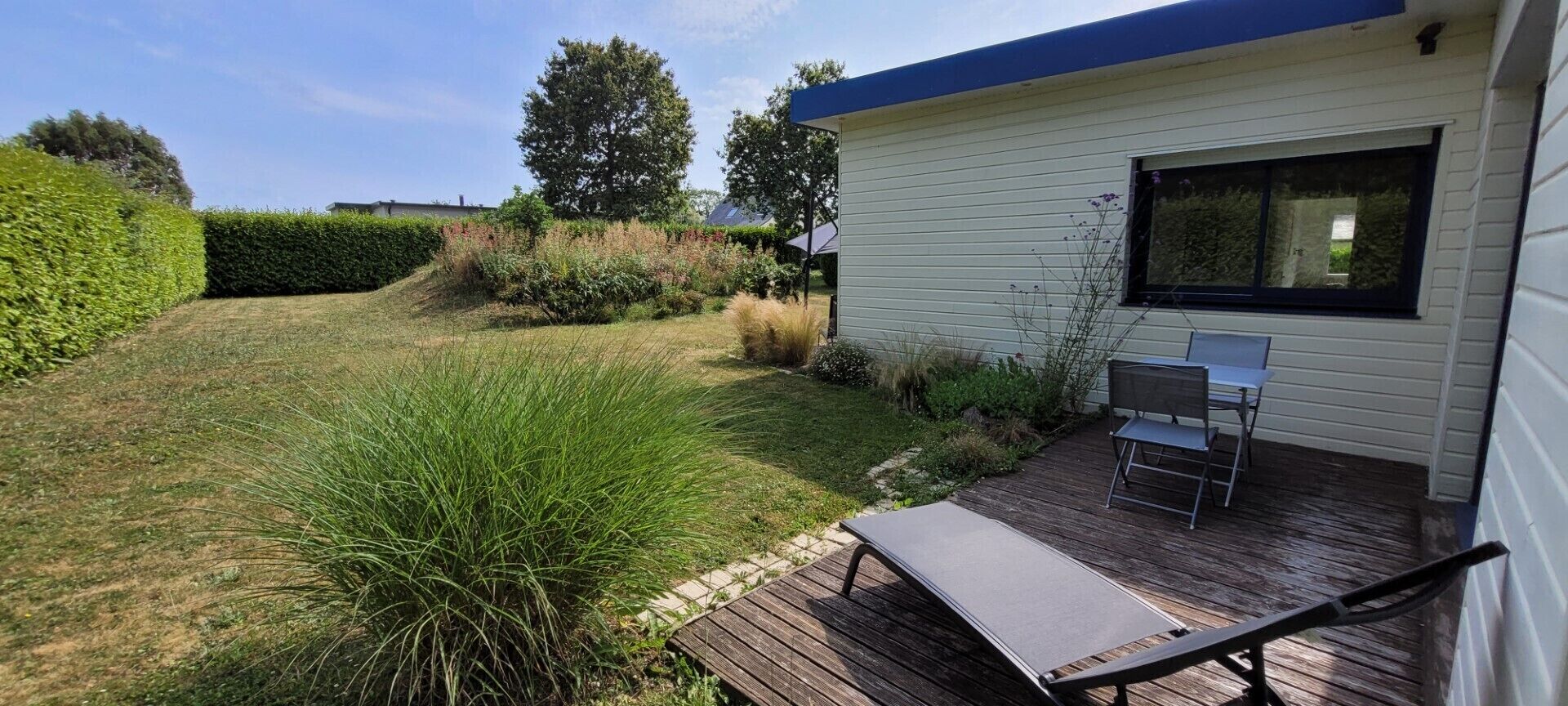 A modern house with a deck, a patio with a table and chairs, and a well-maintained garden.