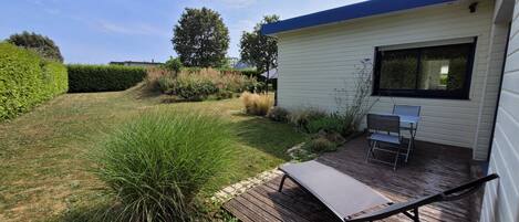 A modern house with a deck, a patio with a table and chairs, and a well-maintained garden.