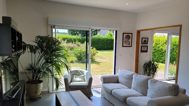 Un salon moderne avec un canapé blanc, une table basse en bois, un téléviseur et une grande fenêtre donnant sur un jardin.