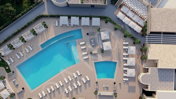 An aerial view of a resort with a large central pool, multiple sun loungers, and a well-maintained garden area.