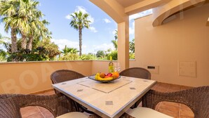 A dining area with wicker furniture, a table with a fruit bowl, and a bottle.