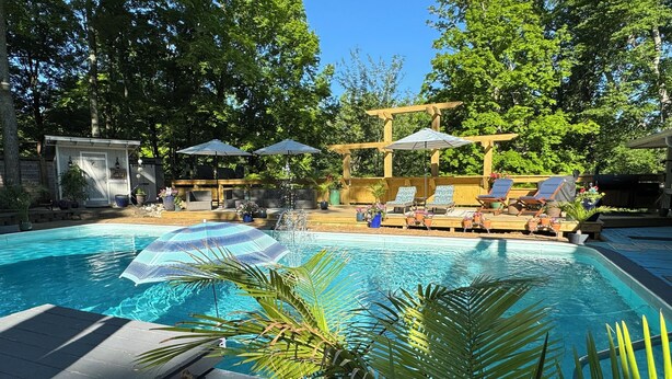 Een zwembad met ligbedden en parasols, omgeven door bomen en een houten pergola.