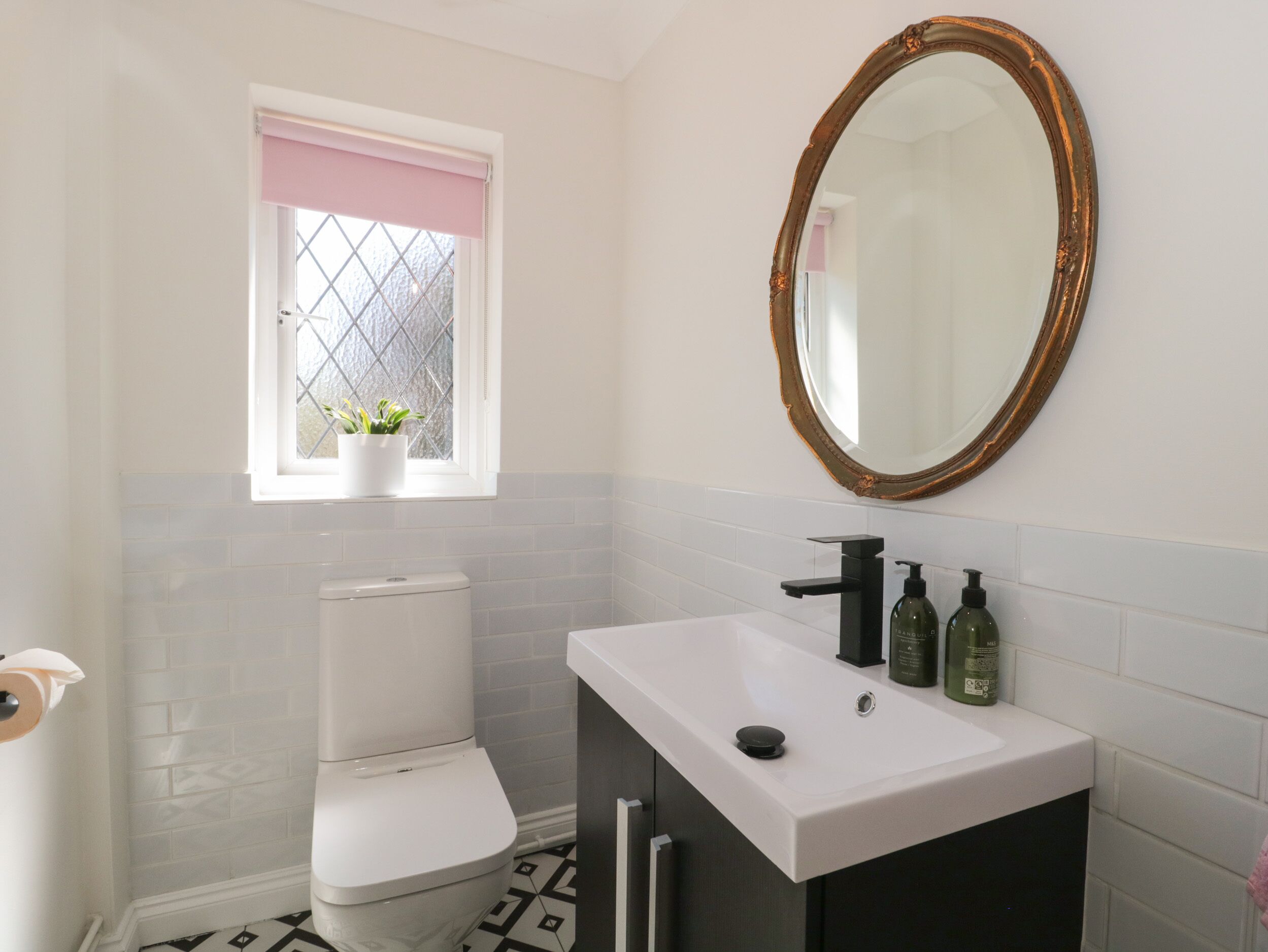 Un baño con inodoro, lavabo, espejo y ventana con planta.