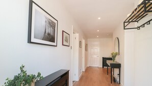 A hallway with wooden flooring, a black console table with a potted plant, and framed artwork on the walls. - 1 Charlotte Close (Poole)