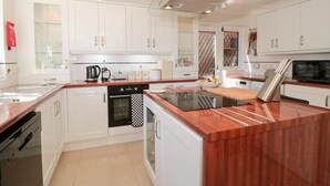 A modern kitchen with white cabinets, a wooden countertop, a glass backsplash, and stainless steel appliances. - 1 Charlotte Close (Poole)