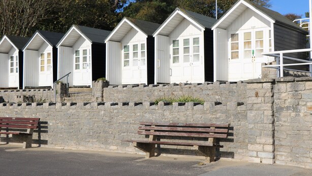 A row of white beach huts with stone walls, wooden benches, and a clear sky. - 1 Charlotte Close (Poole)