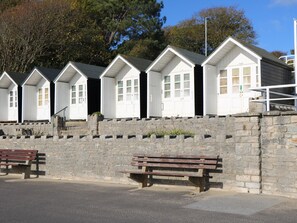 A row of white beach huts with stone walls, wooden benches, and a clear sky. - 1 Charlotte Close (Poole)