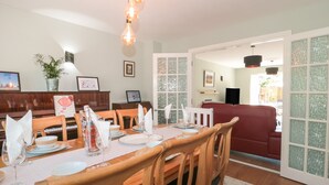 A dining area with a wooden table set for four, surrounded by wooden chairs. There is a piano to the left and a red sofa in the background. - 1 Charlotte Close (Poole)