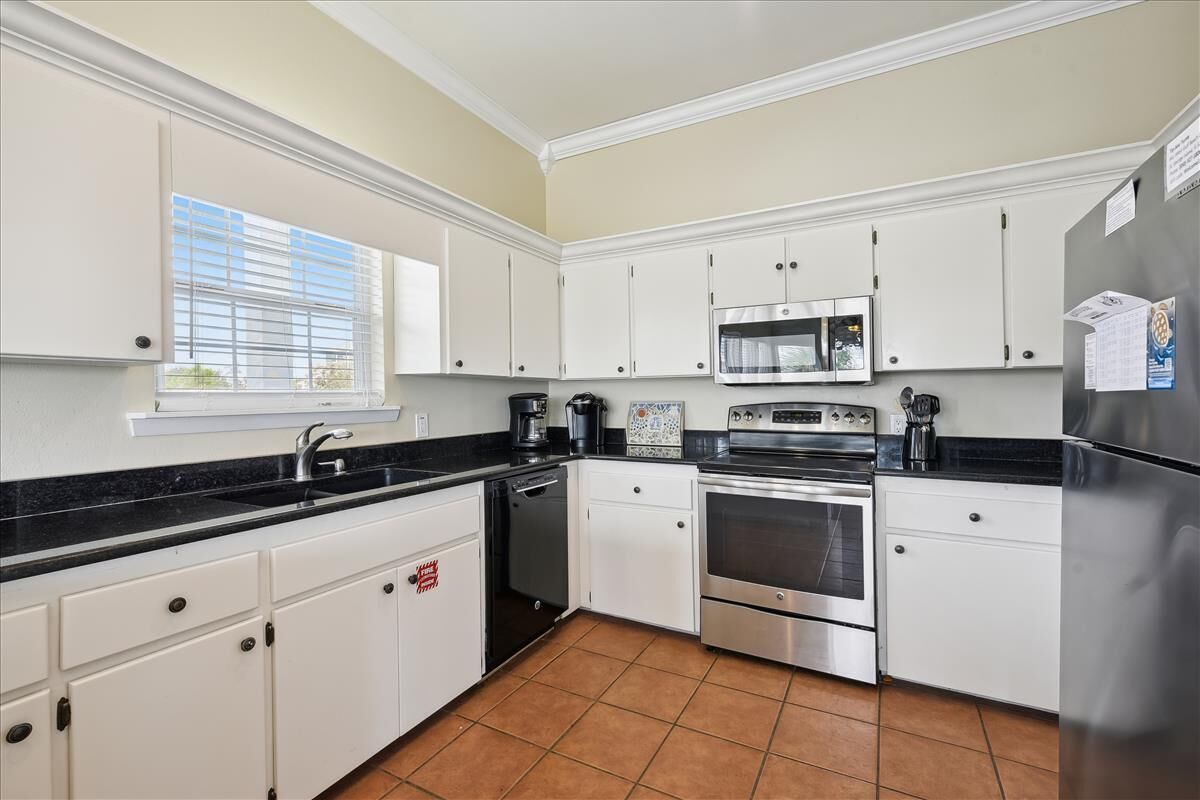 A kitchen with white cabinets, a black countertop, a stainless steel refrigerator, a microwave, an oven, and a dishwasher.
