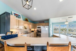 A modern kitchen with a central island, wooden cabinets, and a view through large windows.