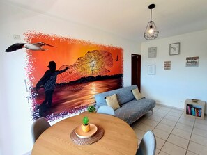 Un salon avec une grande fresque murale, une table de salle à manger ronde en bois, un canapé et une bibliothèque.