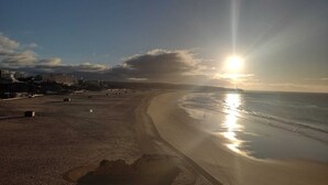 A beach with a clear sky, sun reflecting on the water, and buildings in the background. - Stunning Ocean View! Communal Pool and Quick Walk to the Beach (Portimão)