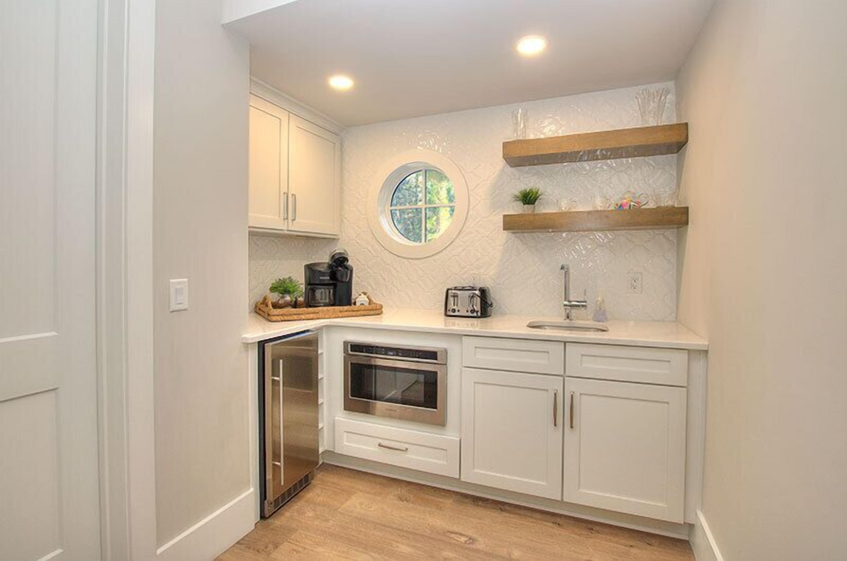 A compact kitchen with white cabinetry, a built-in oven, a dishwasher, and a round window above the sink.