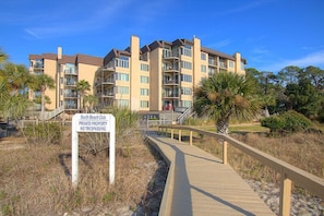 A multi-story building with balconies and a wooden boardwalk leading to it. A sign indicates it is private property with no trespassing.