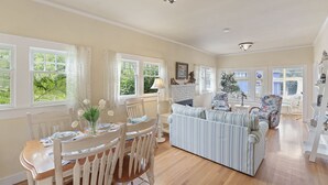 A spacious living room with a dining area, large windows, and a chandelier.