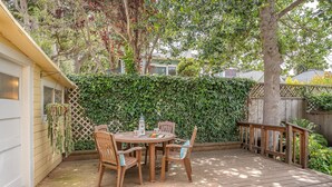 A wooden deck with a table and chairs, surrounded by a wooden fence and a hedge.