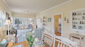 A cozy dining area with a wooden table set for two, a striped sofa, and a vase with white flowers.