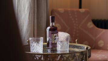 A bottle of Sipsmith gin, two crystal glasses, and a patterned armchair on a table.