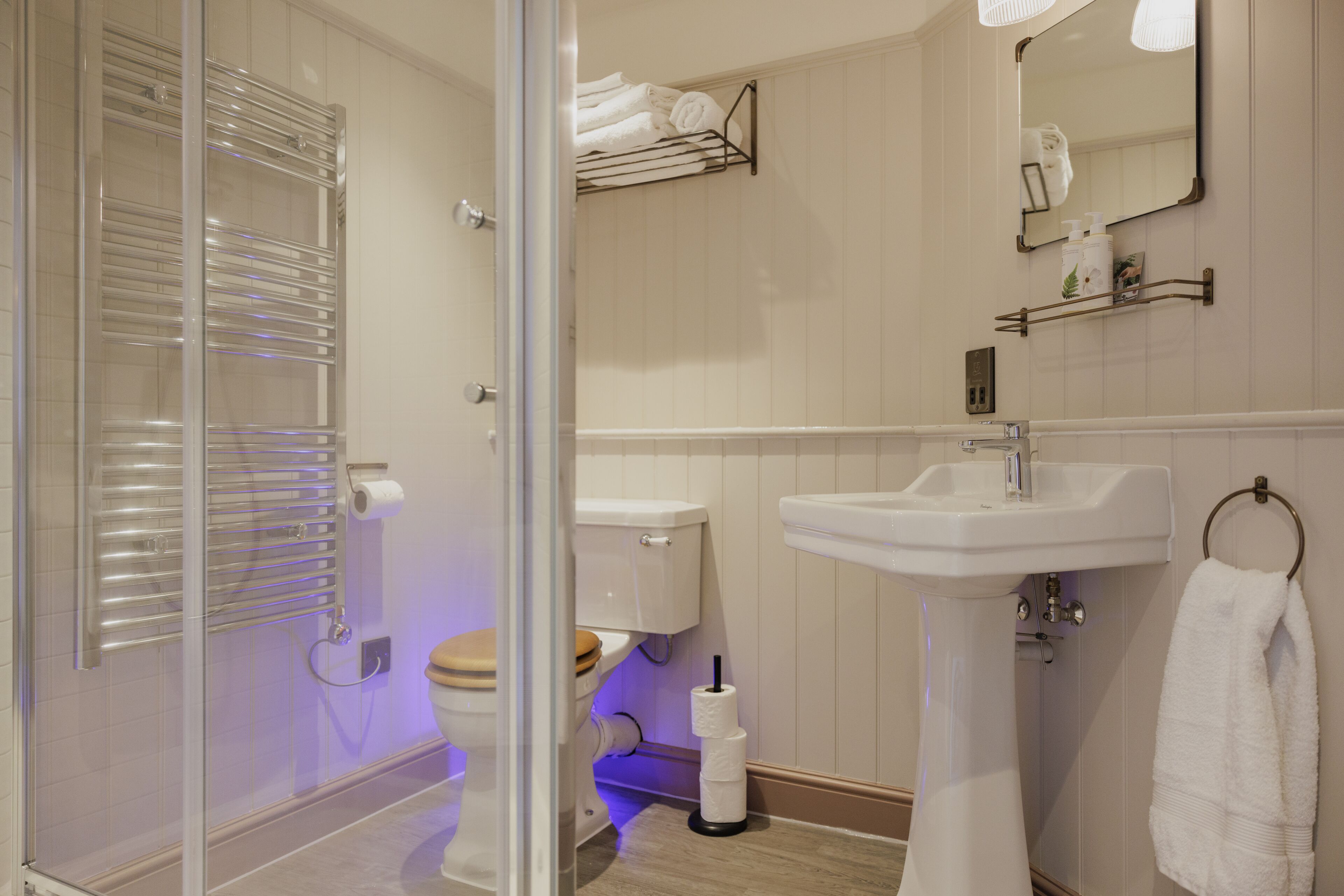 Un baño moderno con cabina de ducha de vidrio, un lavamanos blanco y un inodoro con asiento de madera.