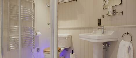 Un baño moderno con cabina de ducha de vidrio, un lavamanos blanco y un inodoro con asiento de madera.