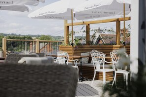 A terrace with white wicker chairs, wooden benches, and umbrellas with text.