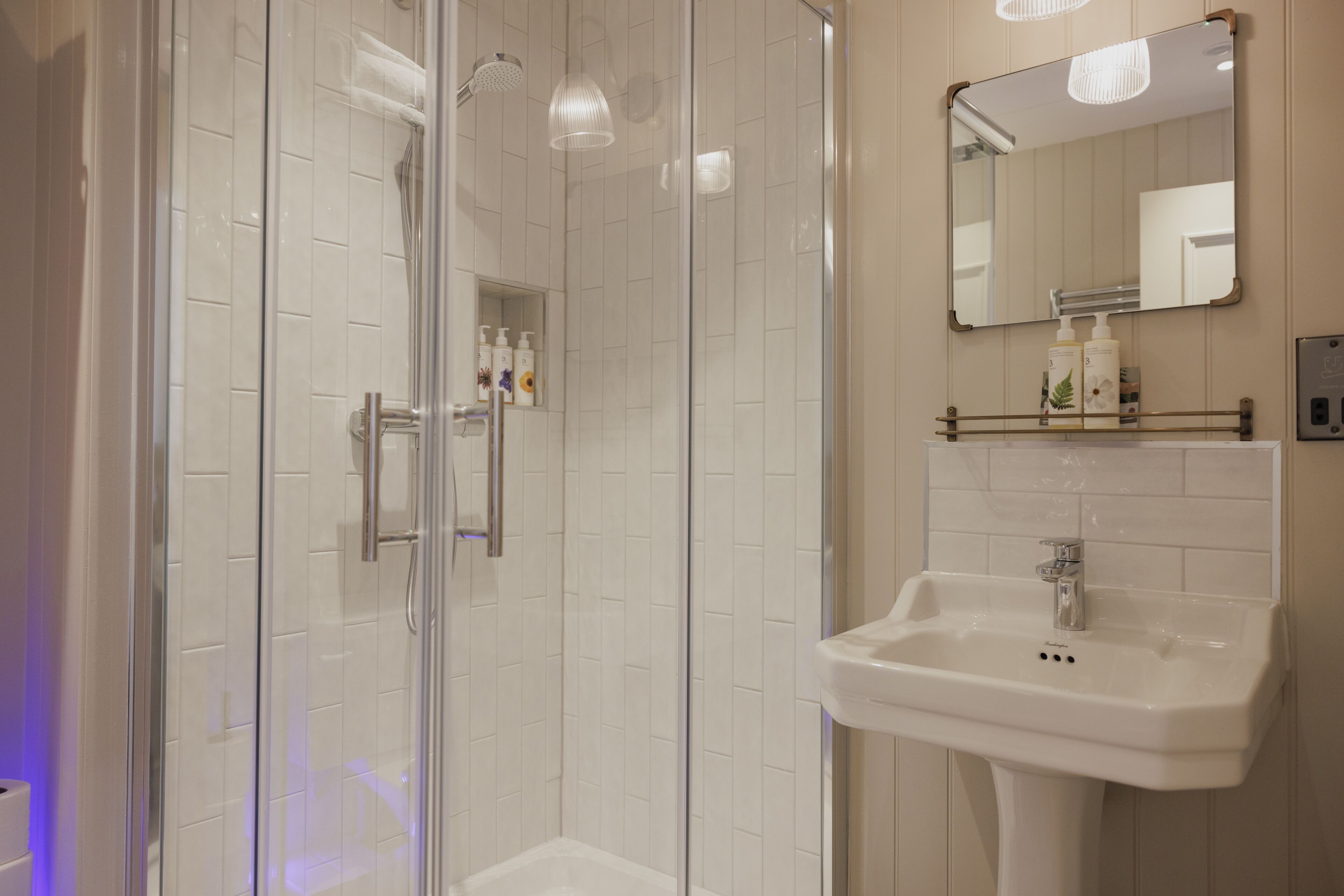A modern bathroom with a glass-enclosed shower, a white sink, and a mirror above it.