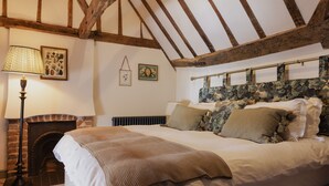 Un dormitorio con una cama grande, chimenea, vigas de madera y papel tapiz floral.