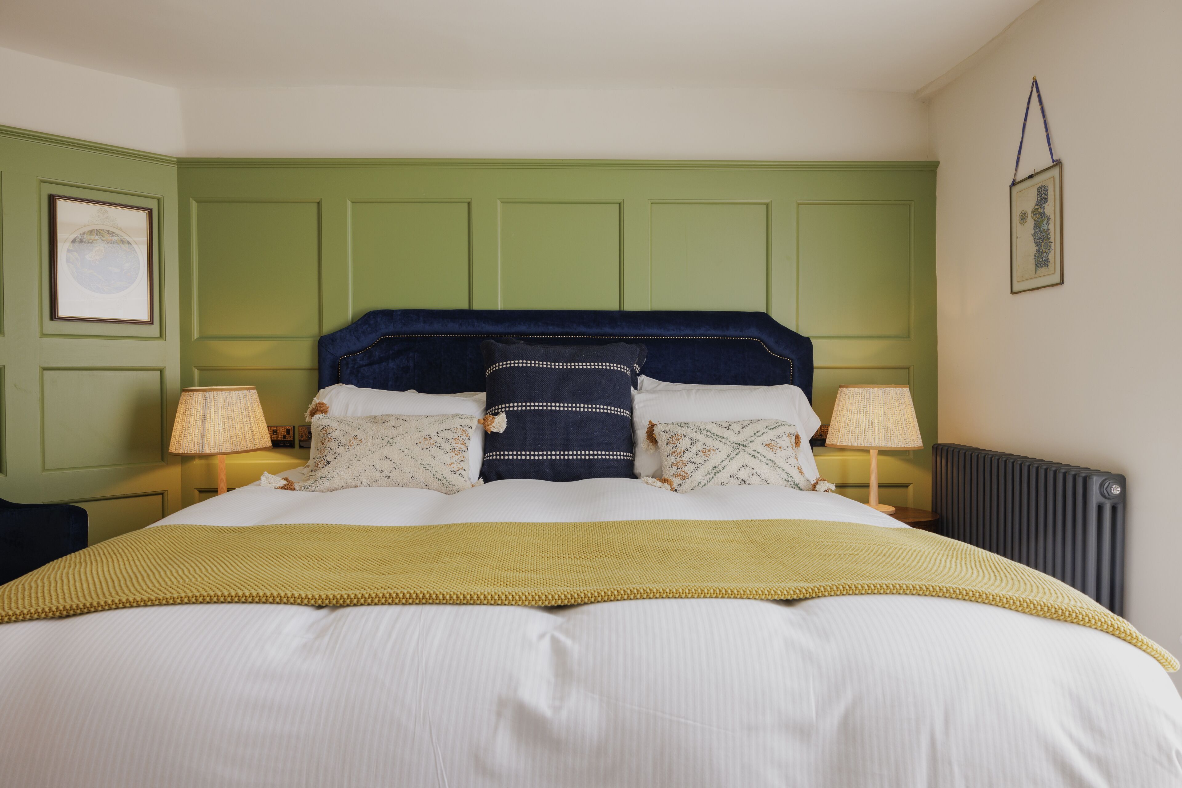 A neatly made bed with a yellow throw blanket, two bedside lamps, and a green headboard.