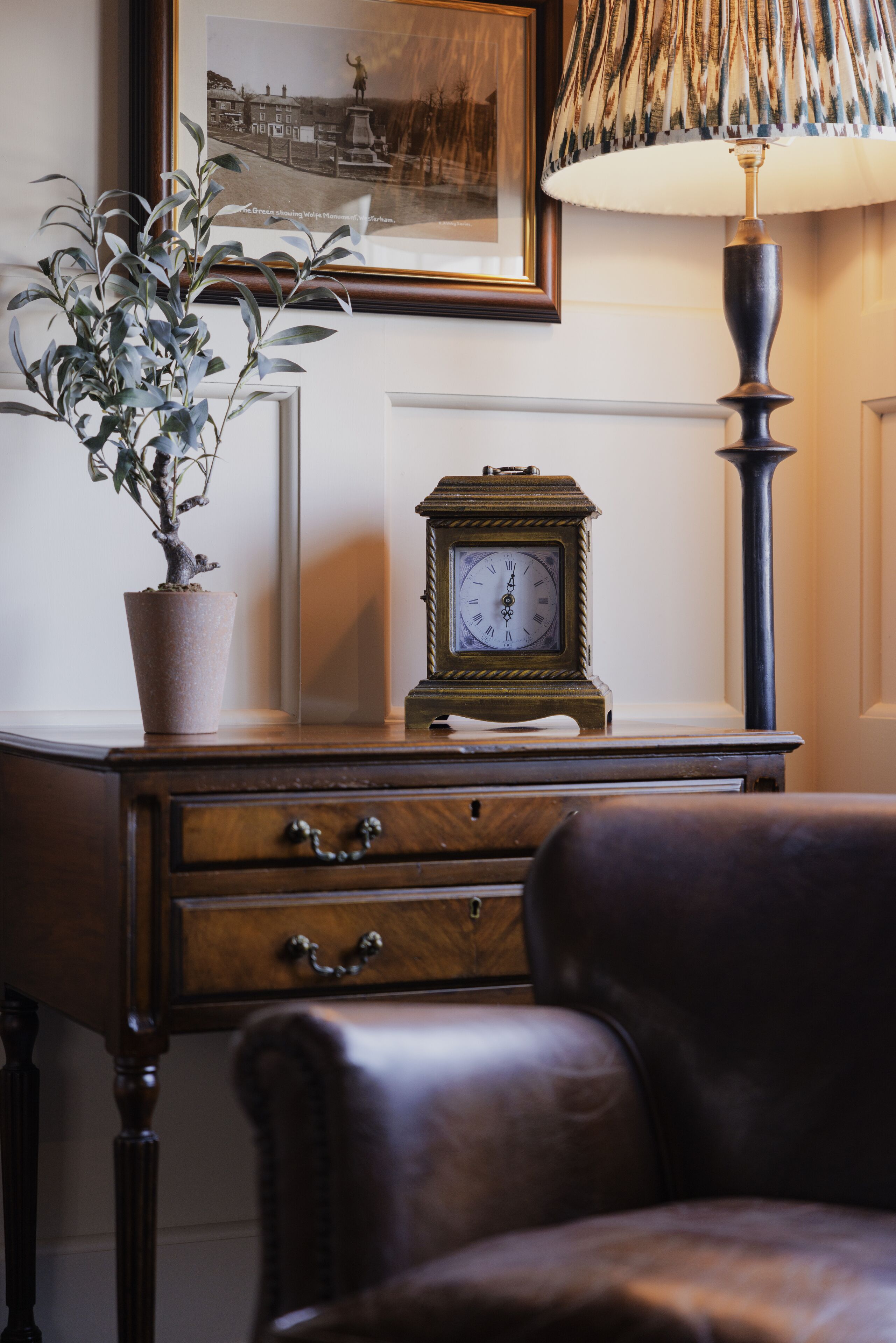A wooden desk with a potted plant, a framed photograph, a clock, and a lamp.