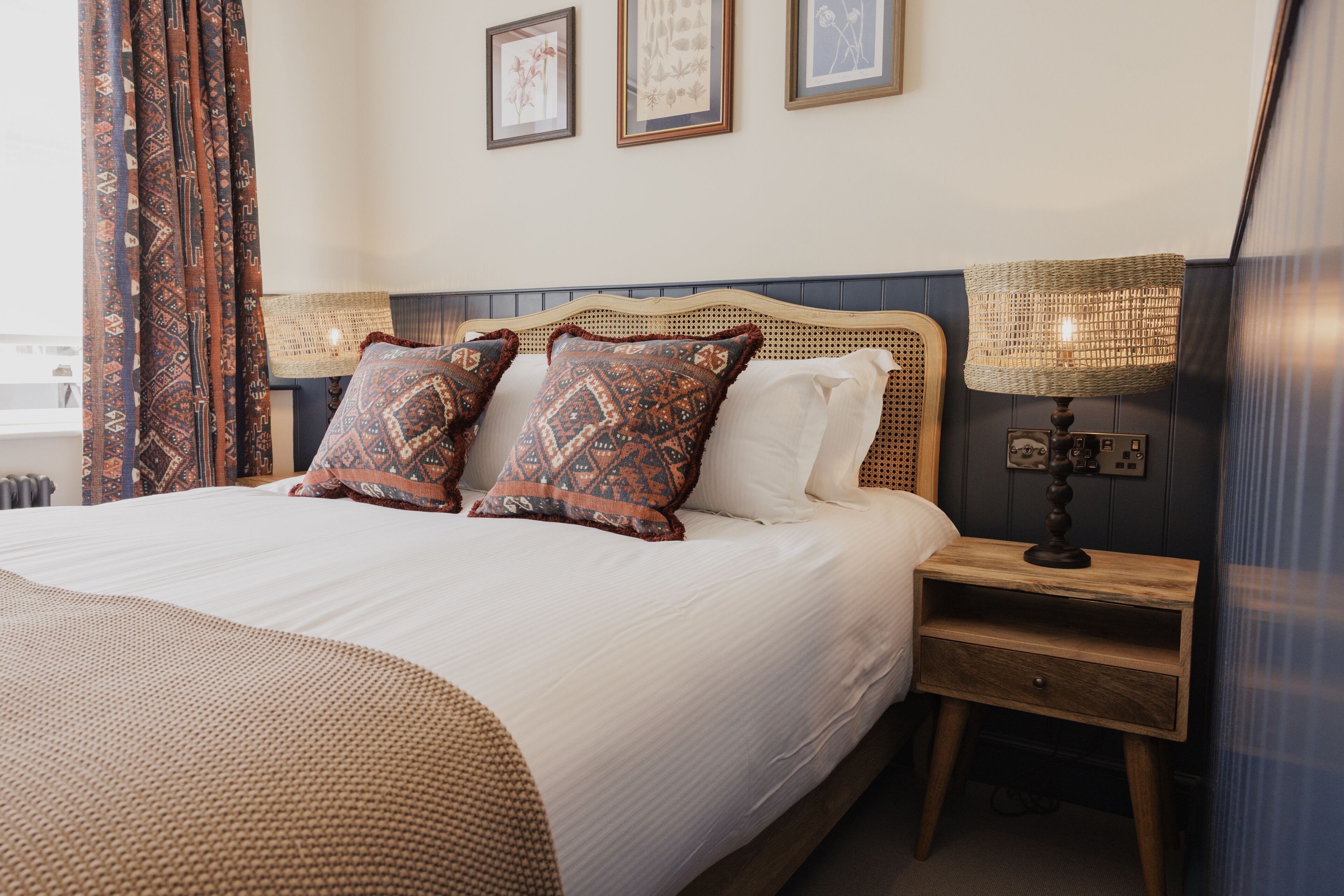 A neatly made bed with patterned pillows, a bedside lamp, and a small wooden nightstand.