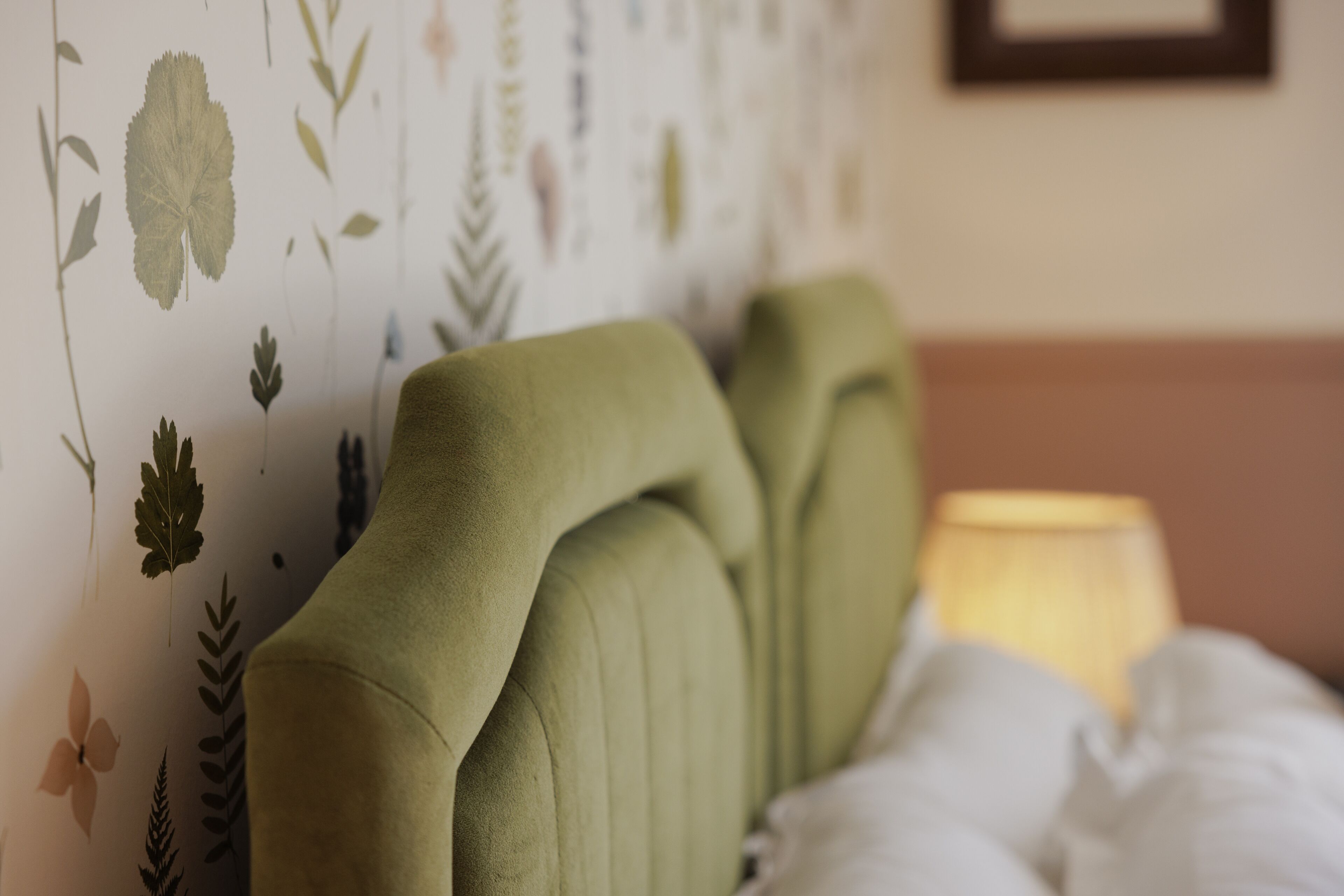A bed with a green headboard and a floral wallpaper pattern.