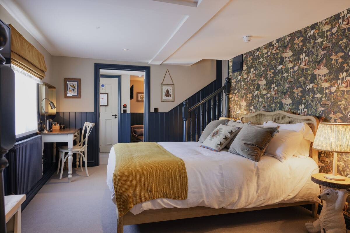 A bedroom with a bed, a desk, a chair, and a staircase.