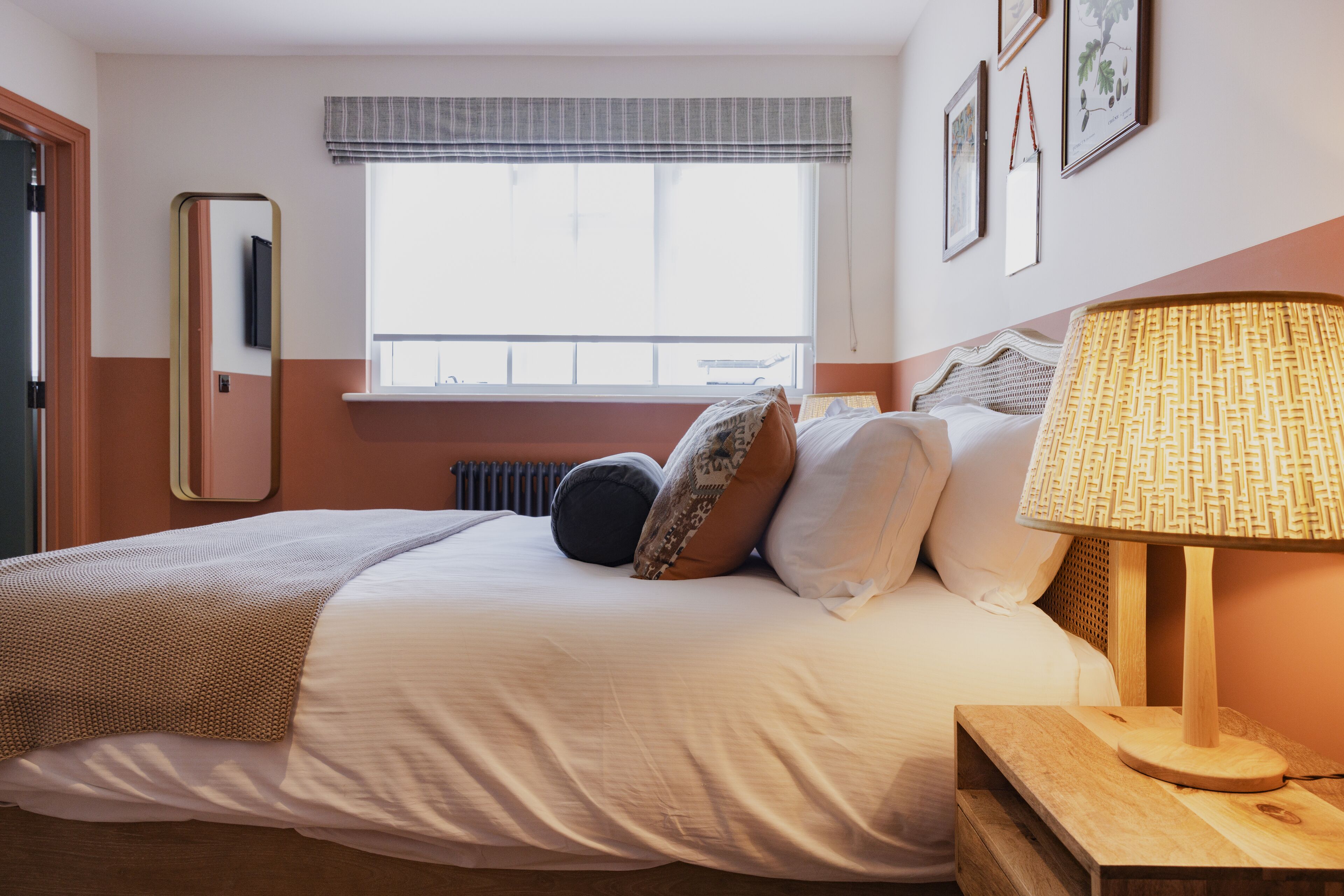 A neatly made bed with a white comforter and pillows, a bedside lamp, and a window with a view of the outside.